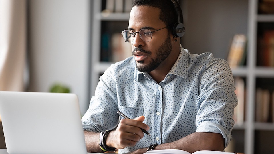 A man, wearing headphones, looking at a laptop.