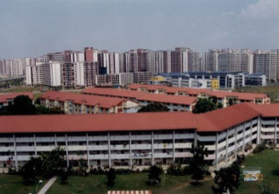 Aerial view of a group of seven four-storey HDB blocks called Punggol Rural Centre in Sengkang. In the background is a sea of high-rise HDB flats.