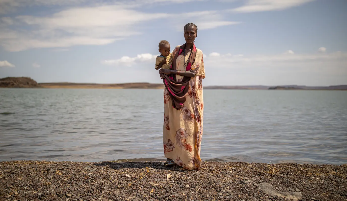 Marin Lemotou holds her one-year-old against the backdrop of Lake Turkana.