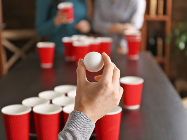 A woman about to throw a ping pong ball in the Beer Pong Drinking Game