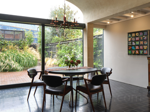 Stylish dining room featuring large windows with garden view and circular grey dining table with matching chairs Skype background