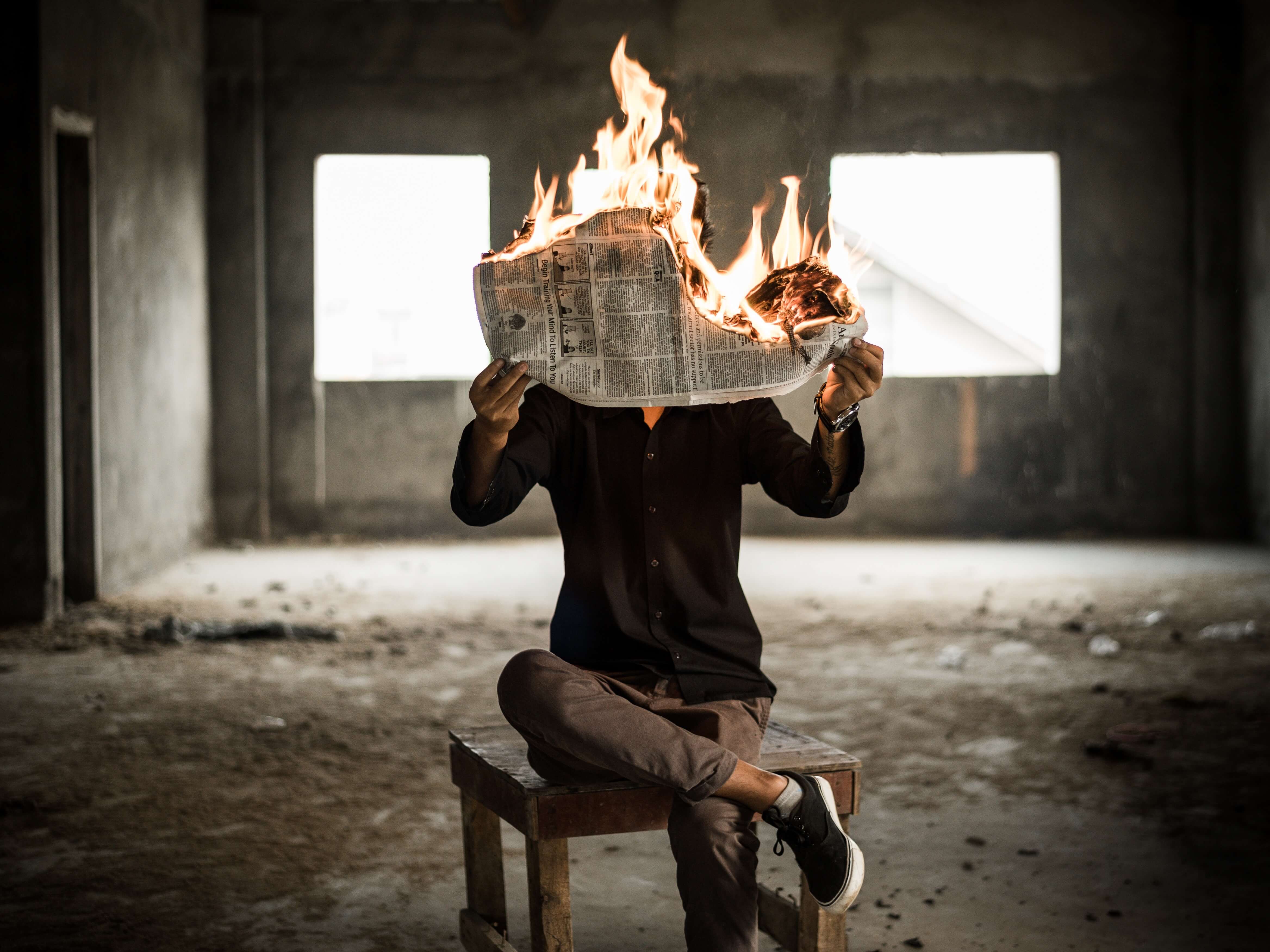 Man sitting on chair, holding newspaper on fire