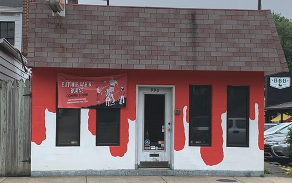 small cinderblock building with a black roof, white walls, and red paint that looks like dripping blood with a white banner that says butcher cabin books