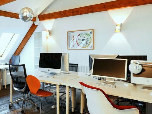 Contemporary loft style office workspace featuring prominent wooden beams over wooden computer desks and assorted chairs Microsoft Teams background