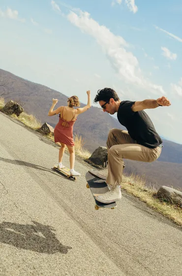 Photograph of a man and a woman skateboarding outdoors on a warm day