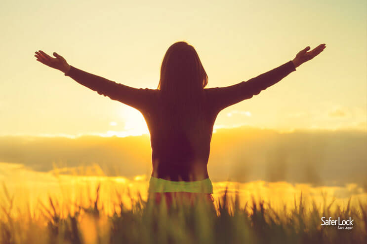 Photo of a woman with her arms reaching out as she looks at a yellow sunset.