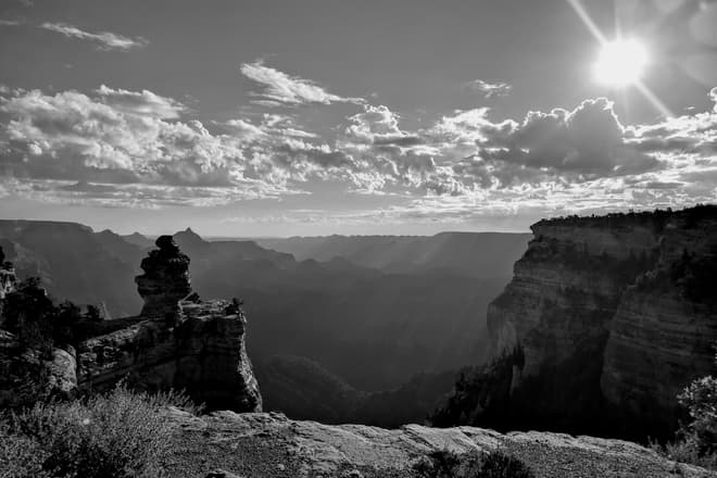 A black-and-white photograph of the Grand Canyon shortly after dawn. Thick haze obscures the far side of the Canyon. In the foreground, a pillar of rock rises out of the South Rim.