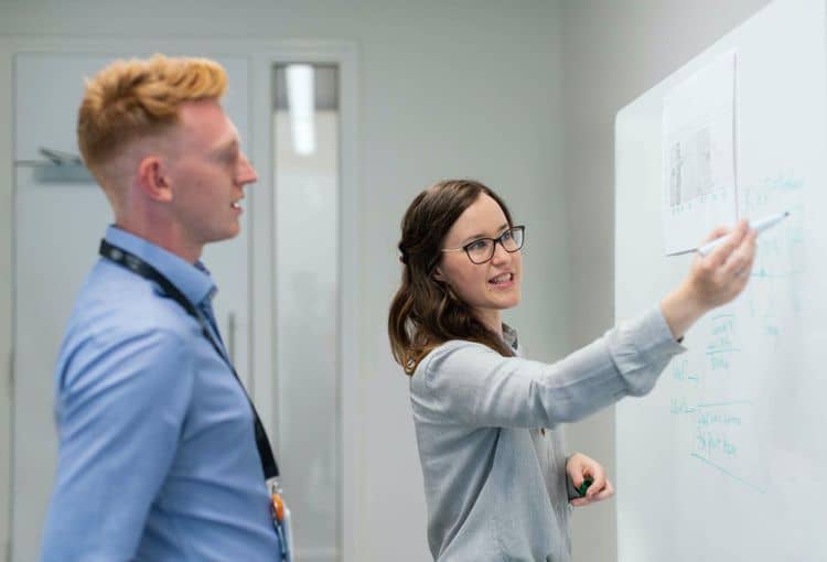 Trainerin an Whiteboard Trainerin erklärt Kursteilnehmer Übung an Whiteboard während einer Firmenschulung