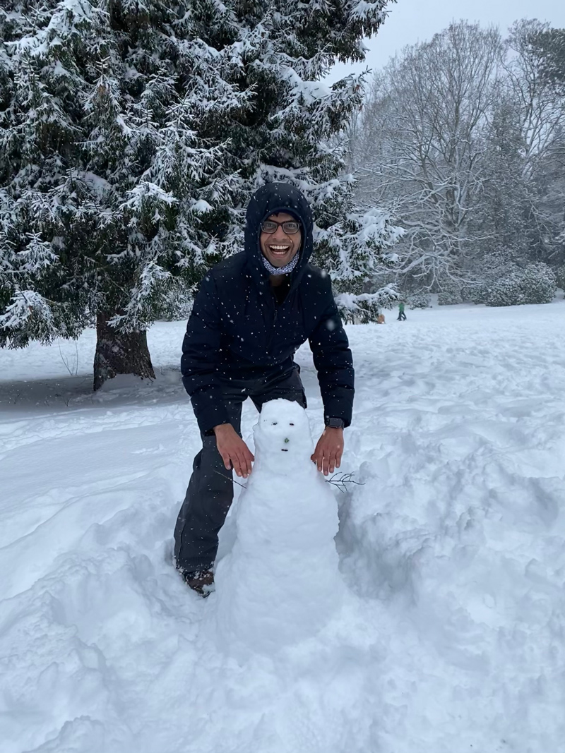 A man in a puffy coat grins while placing his hands on the proverbial shoulders of a goofy-looking snowman