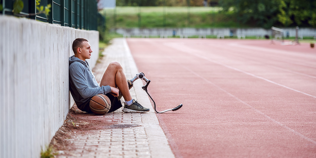 Athlete with a prosthetic leg, sitting at the edge of a running track. Athlete with a prosthetic leg, sitting at the edge of a running track.