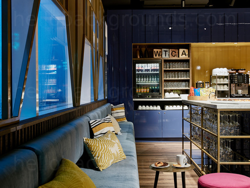 Artistic modern bar interior featuring long padded blue bench seating next to triangular shaped windows and drinks fridge  Zoom background