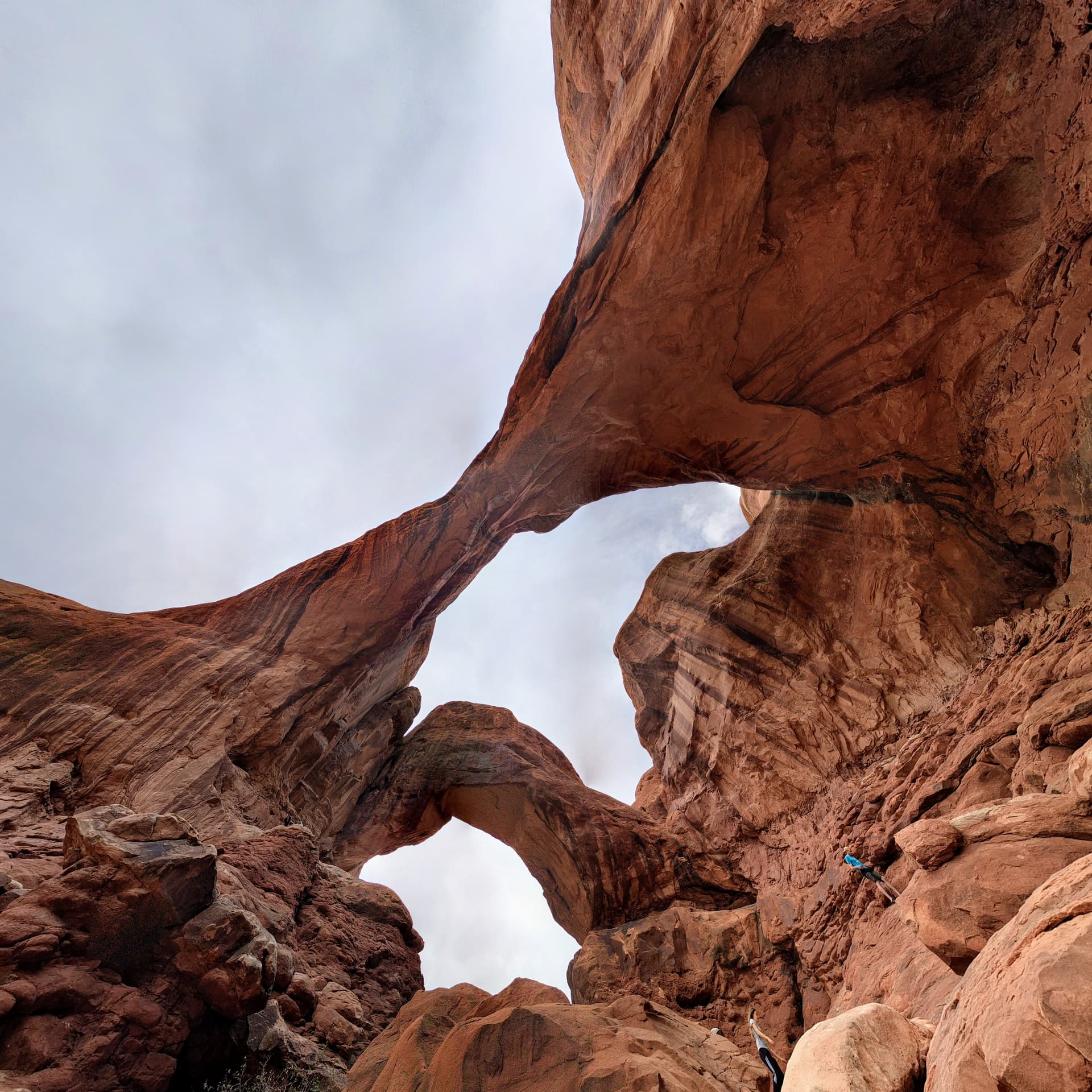 A wide-angle photograph looking up at Double Arch in Arches National Park. Both arches can be seen, almost at right angles to each other, with the closest arcing almost directly overhead.