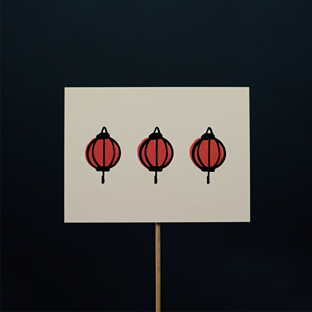 Doodles of three identical red paper lanterns with a slight offset. The paper is mounted on a thin wooden stick against a black background.