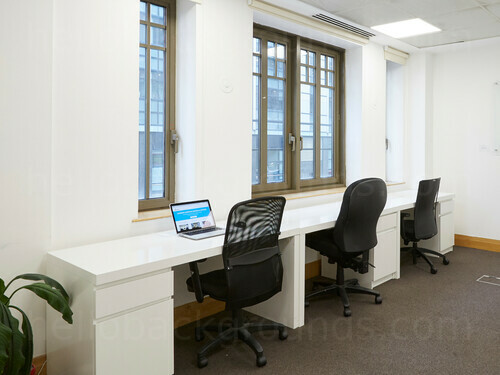 Effortless shared workspace with classic style windows behind long white multi-desk and black office chairs  Zoom background