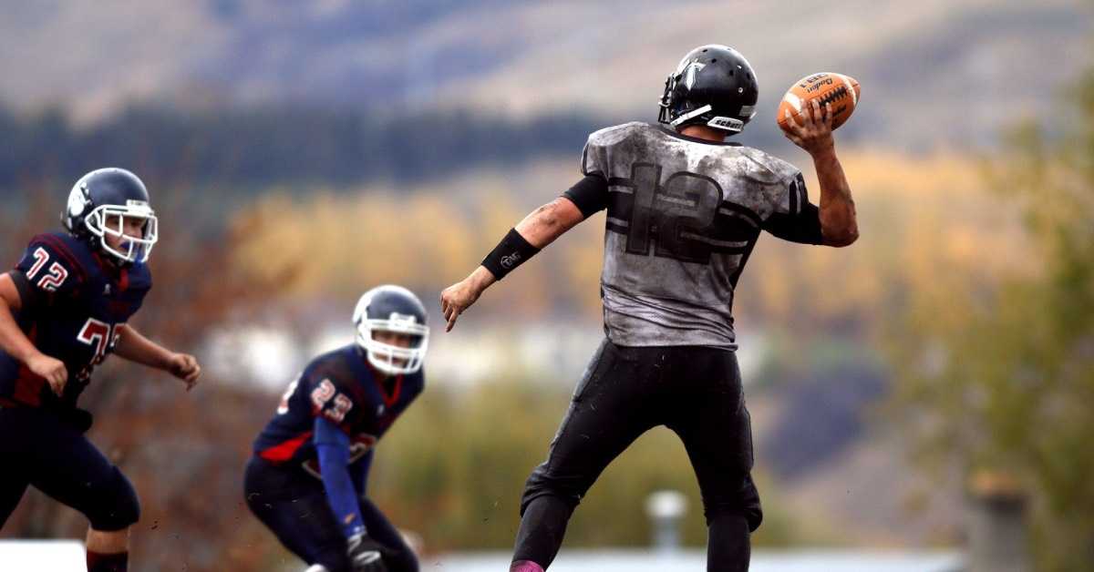 Ein erwachsener American Football Spieler trainiert zwei Jungs draußen auf dem Feld