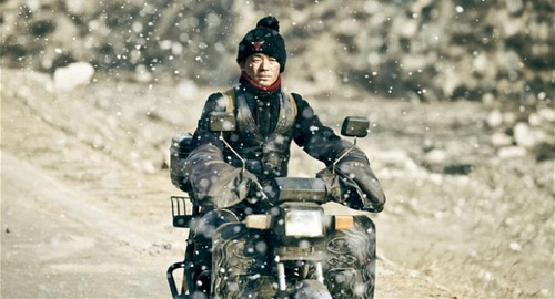 A screenshot of San'er, a young man wearing a Chicago Bulls beanie, riding a moped in snowfall. From the movie 'A Touch of Sin'.