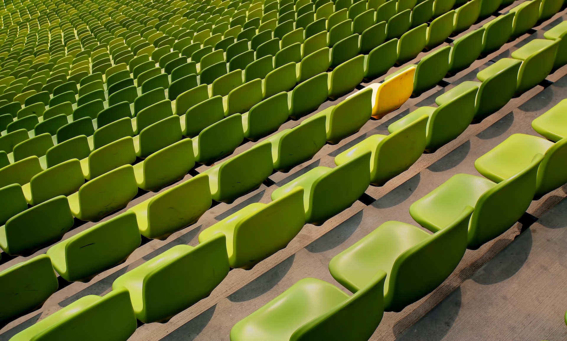 A single yellow chair among a sea of green chairs.