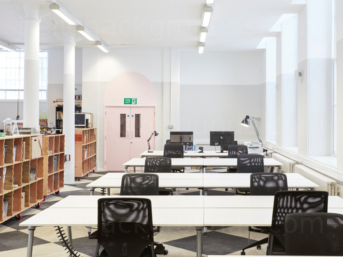 Well lit classic style shared workspace containing white multi-desks with black office chairs  next to wooden book shelves  Skype background