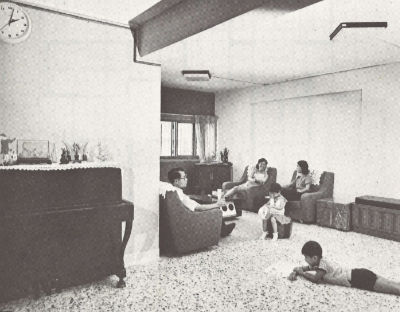 A black and white photo of a family of five resting in the living room of their five-room HDB flat.