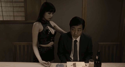 An animated gif of a scene from the film 'R100' of a woman in leather clothes smashing a man's sushi with the palm of her hand.