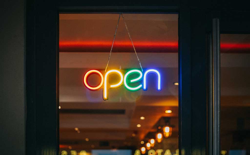 A neon sign of the word open in different colours, photo by Viktor Forgacs on Unsplash