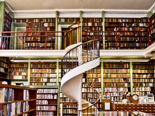 Library interior featuring two-story view of bookcases containing books behind spiral white staircase Zoom background