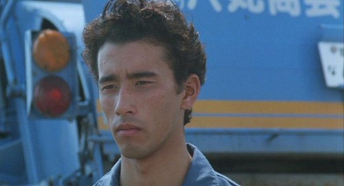 A close-up screenshot from the film 'A Scene at the Sea' of a young man, Shigeru (played by Claude Maki).