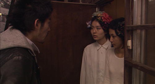 From the film 'Kakera: A Piece of Our Life', a screenshot of a man outside of an apartment and two young women standing in the doorway looking sternly at him.