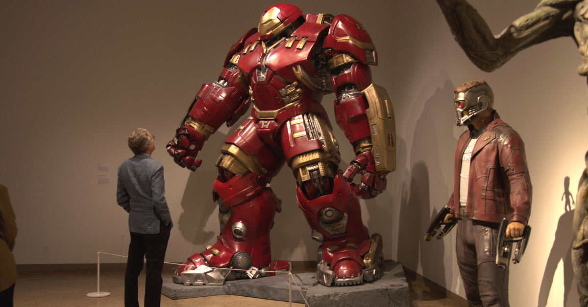 Man standing next to Hulkbuster armor statue and Starlord from Avengers: Infinity War. 