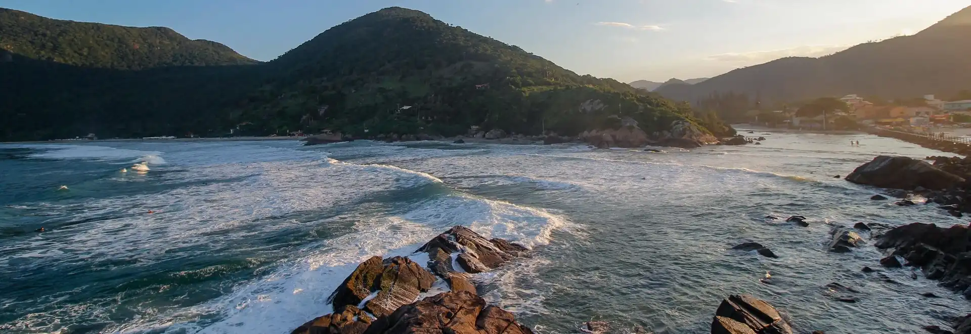 Vista de dentro do mar para praia pegando pedras no meio do mar e montanhas ao fundo