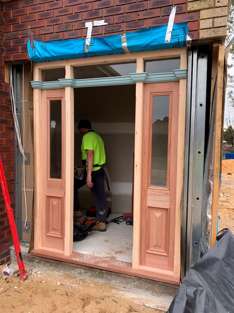 Work in progress on fitting a new ornate timber frame for a home's front door.