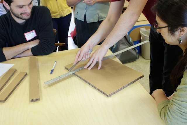 Students around a table while Molly scores a piece of cardboard with the blunt end of a fork.