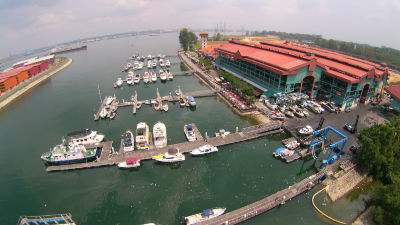 An aerial view of the Marina Country Club at Punggol. Many yachts and boats are moored along five floating docks in the calm green waters of Punggol River.