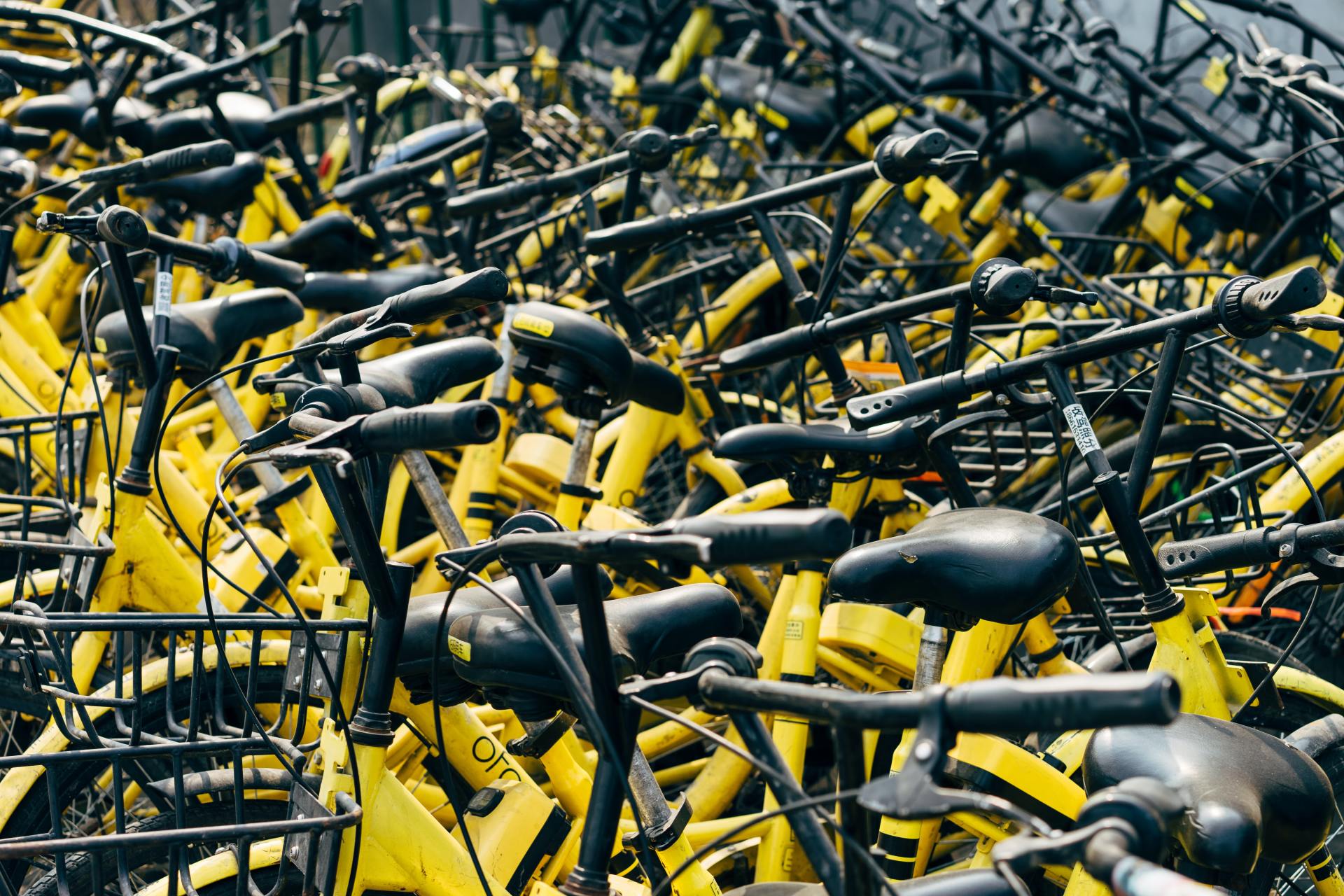 Several yellow bikes with baskets standing next to each other placed  in an urban area.