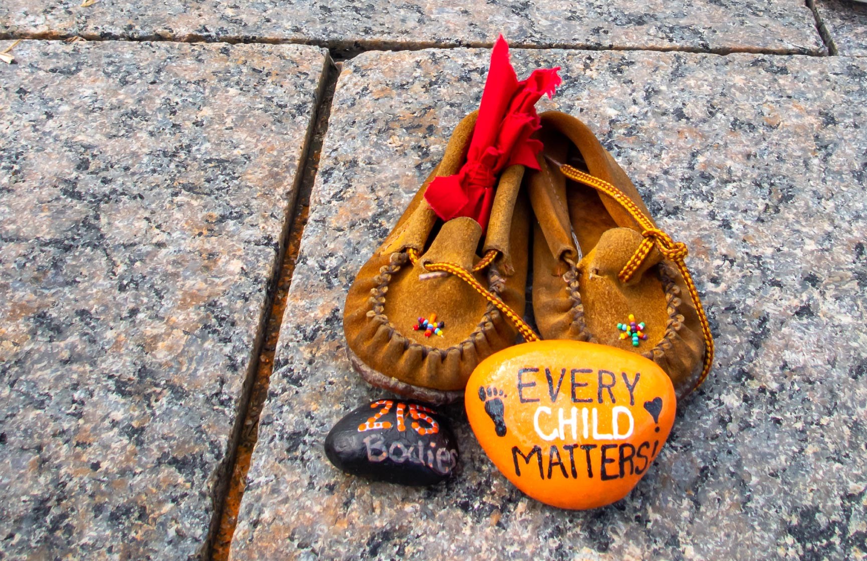 Children's shoes and a painted orange rock that reads &quot;Every Child Matters&quot; site at a memorial at Canada's Parliament Hill for Indigenous children who were sent to Residential Schools