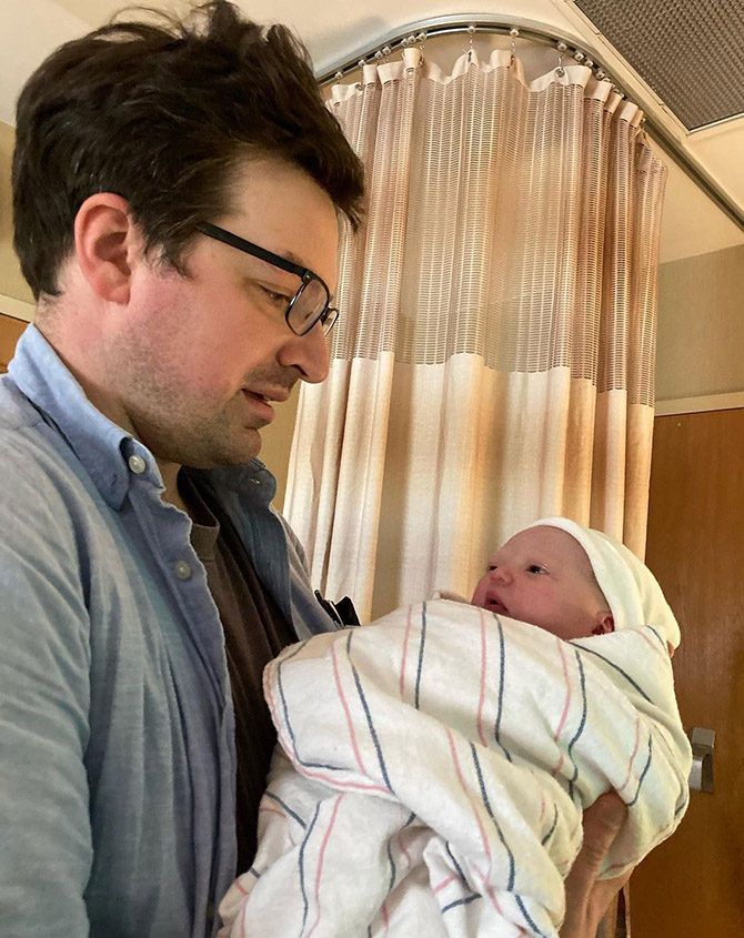 A tired looking man holds an infant wrapped in a hospital blanket
