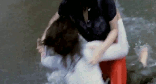 An animated gif of a scene from the film 'Girl Boss Guerilla' of 2 female gangsters wrestling on the beach as the tide comes in.