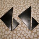 Four shiny black tangram triangles arranged in pairs of small and large together make two six digits. They are resting on a floral petal patterned cushion.