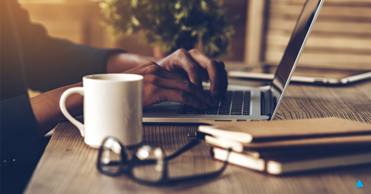 A man works on his laptop with a cup of coffee in the foreground.