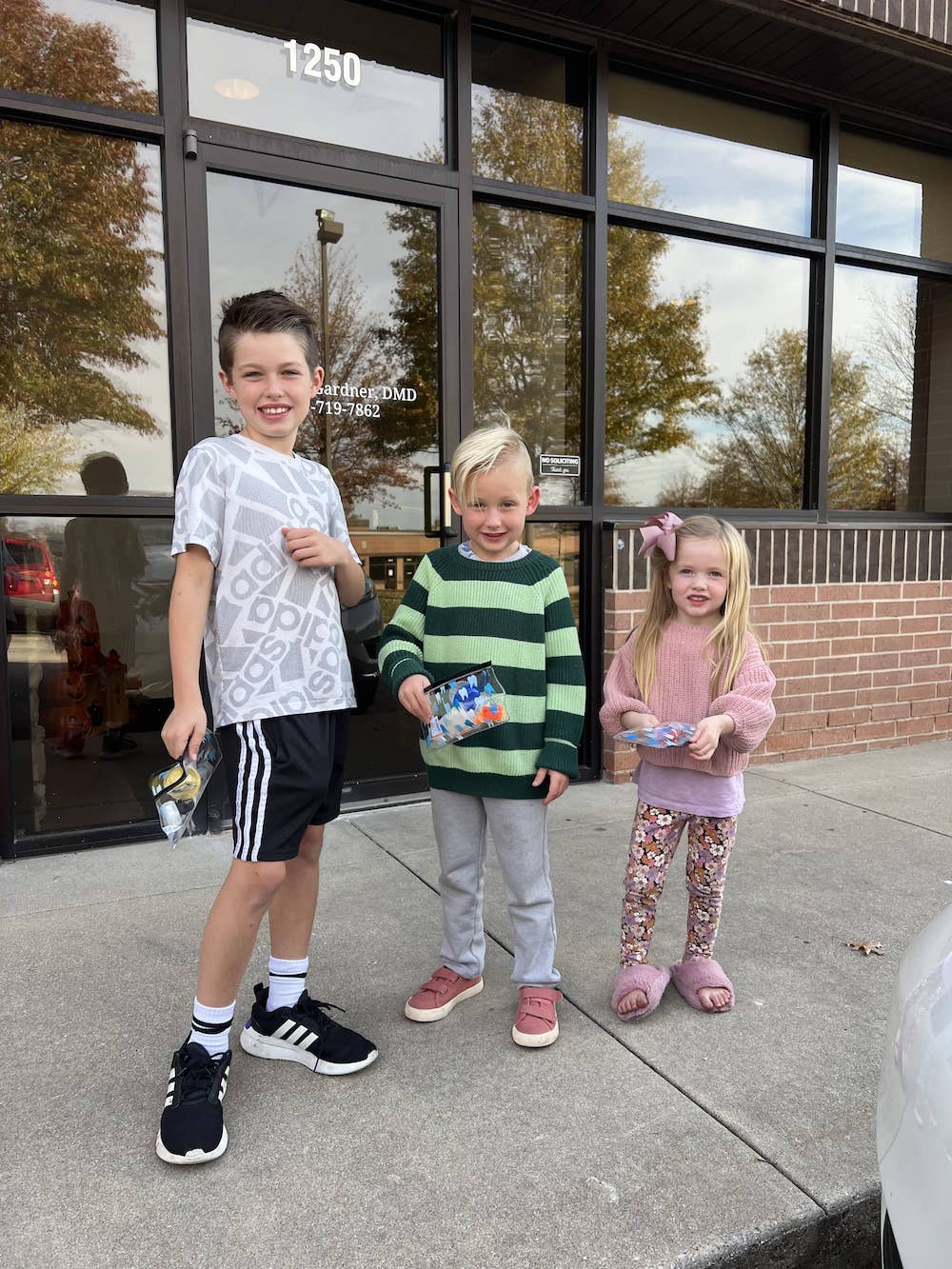 Three kids standing next to each out outside of a store.