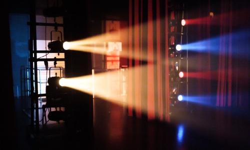 Thumbnail Spotlights on side booms with red and blue colour gels illuminating the backstage of a stage, smoke/haze around the lights.