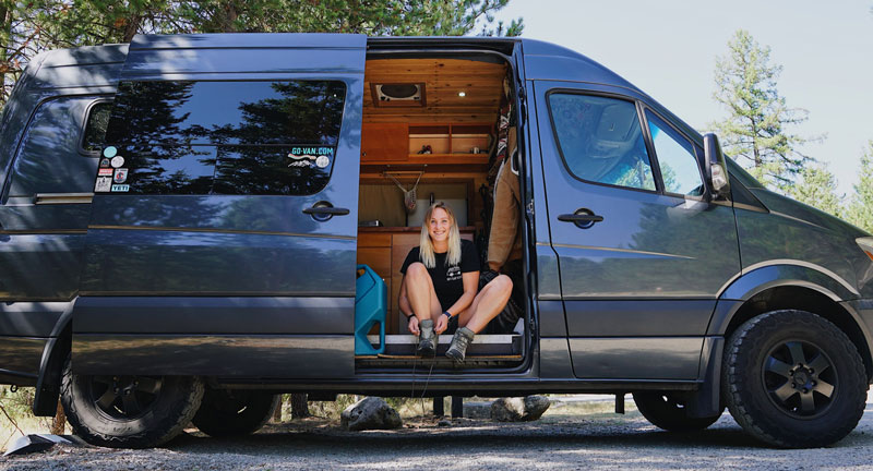 Van Life Katie Larson putting on hiking boots in her van at a primitive campsite