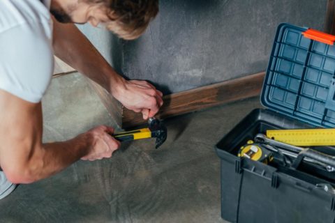 craftsman hammering nail into baseboard