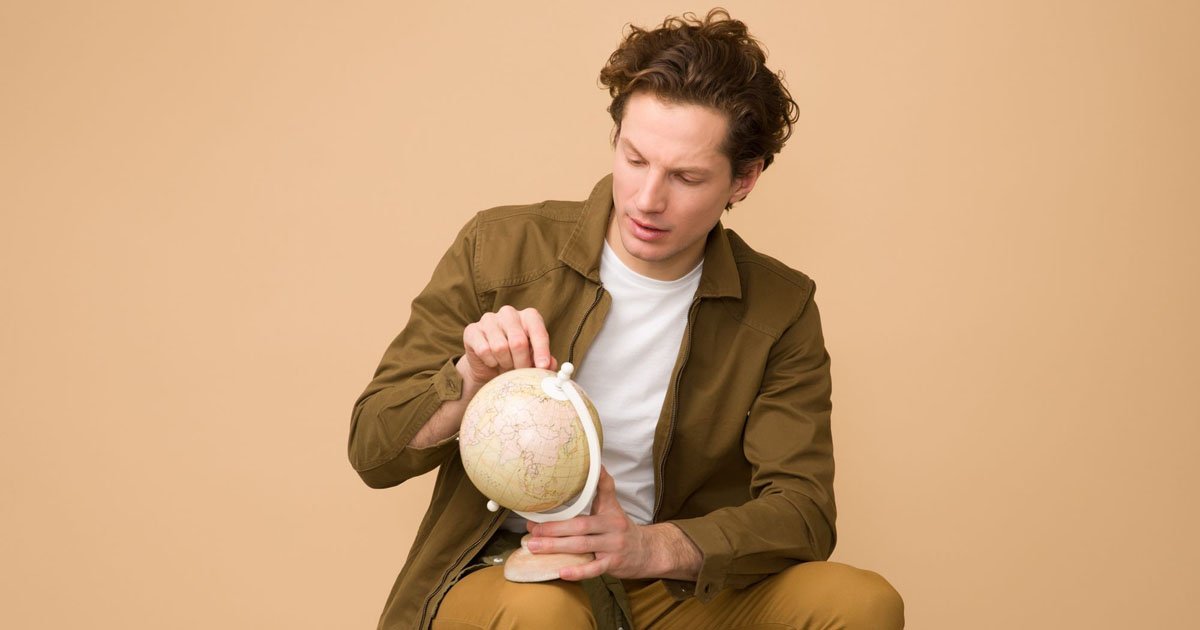 a sitting young man pointing at a globe curiously 