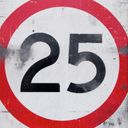 A battered reflective speed limit sign. The speed limit is twenty five.