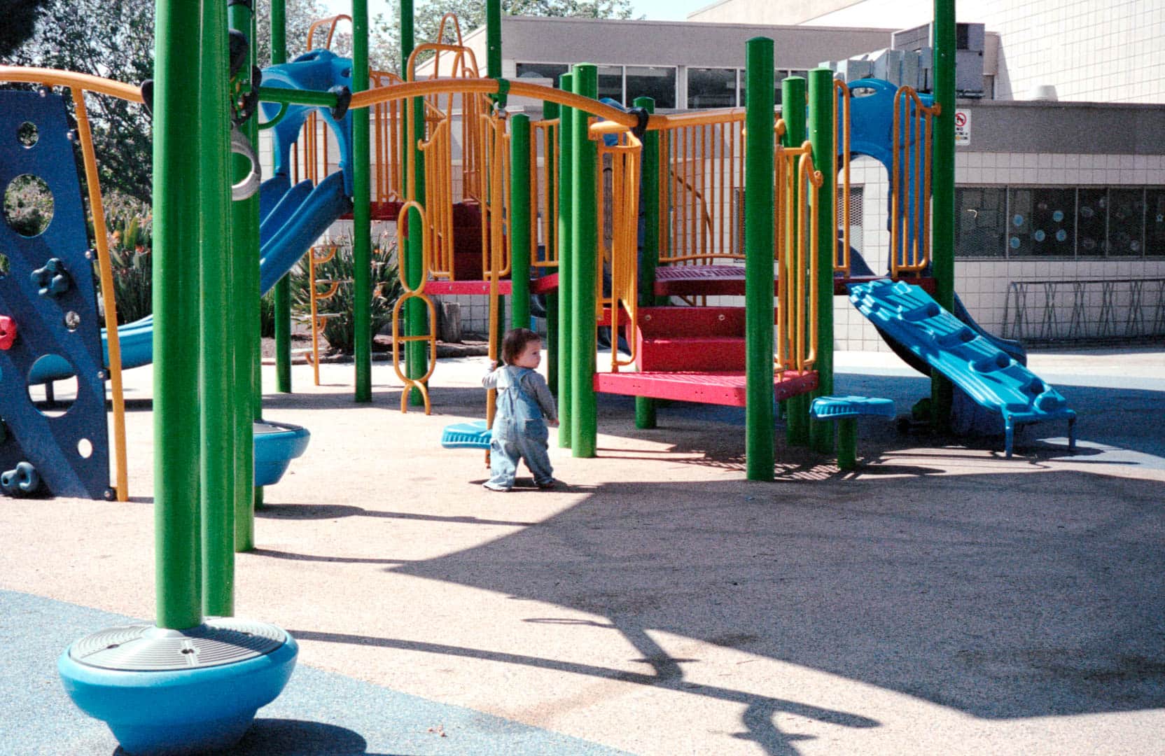 A young toddler standing in the middle of a largely empty playground