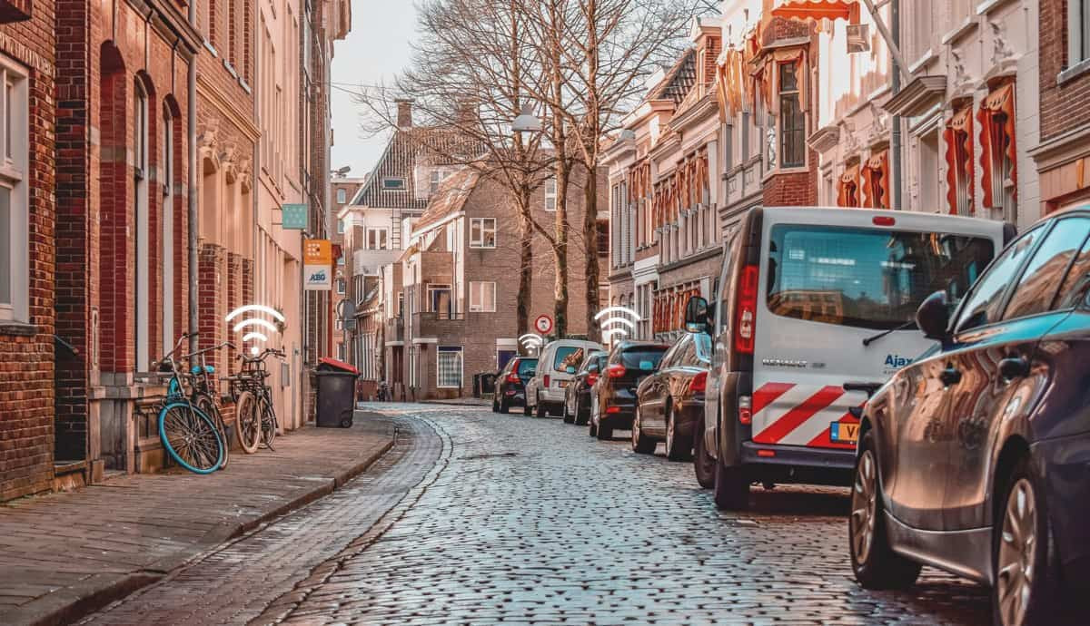 Three wifi-animated icons placed above bikes and cars who are parked on a calm European alley.