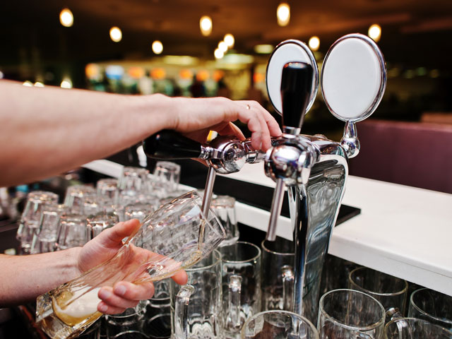 A bartender pouring draft beer from a tap in a bar with clean beer lines