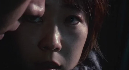 A close-up screenshot of Rei (played by Shinobu Terajima) with tears in her eyes looking into the eyes of a man.