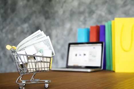 Photo of Small Toy Shopping Cart with Money inside and a laptop in the background.